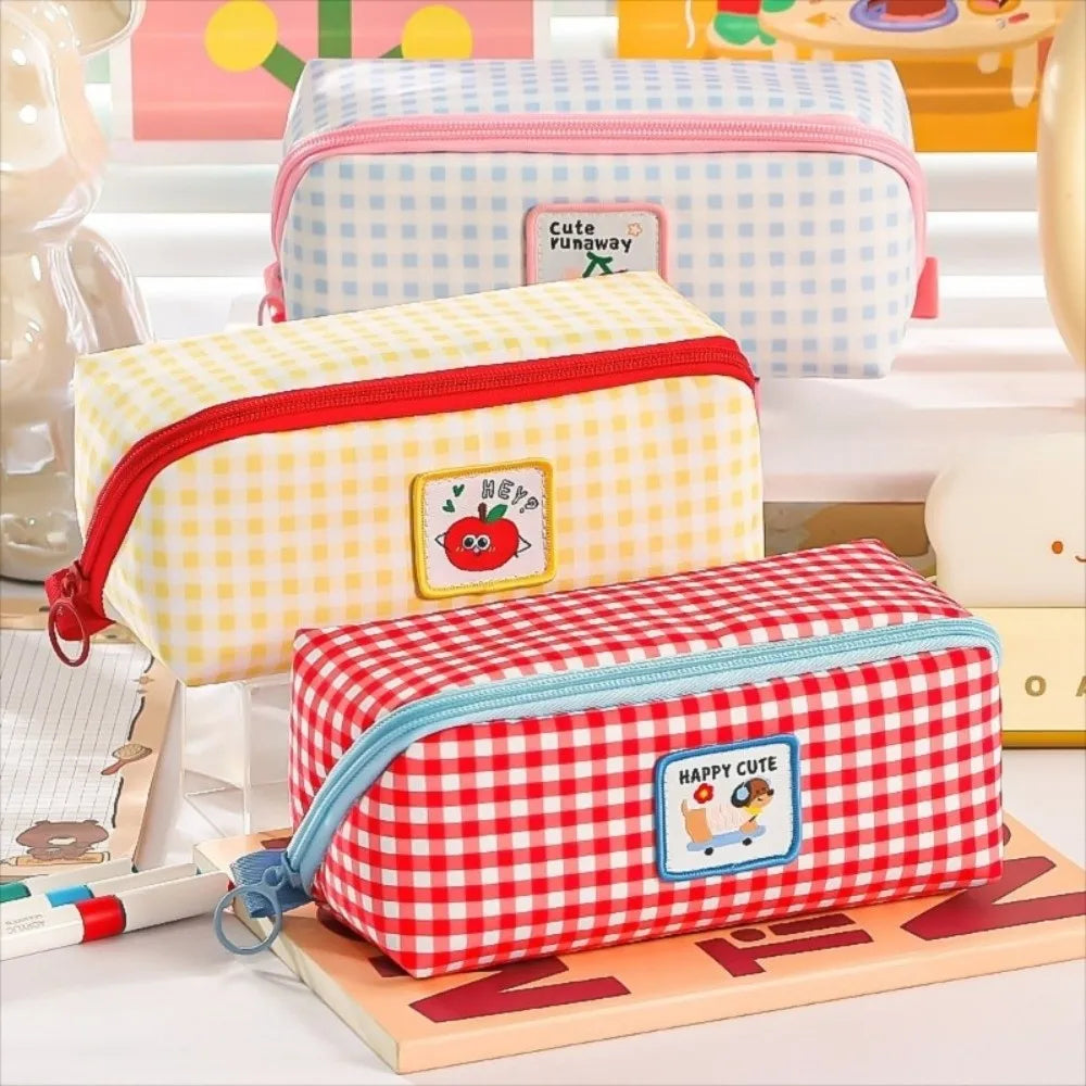 Three colorful checkered kawaii pencil cases with cartoon designs on a wooden surface.