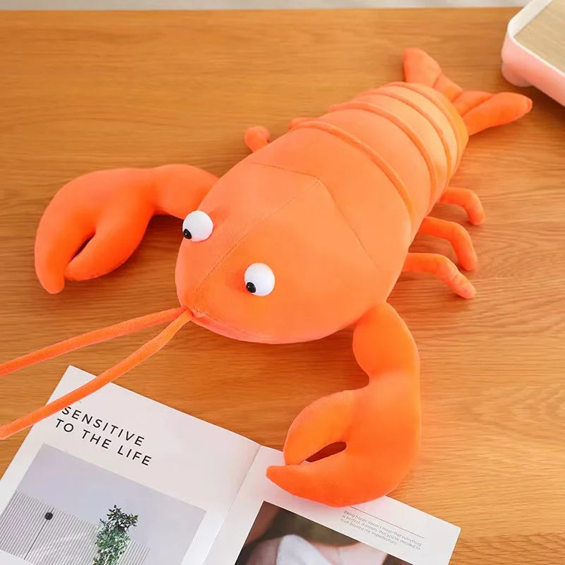 Kawaii plush lobster toy on a wooden surface with a magazine underneath