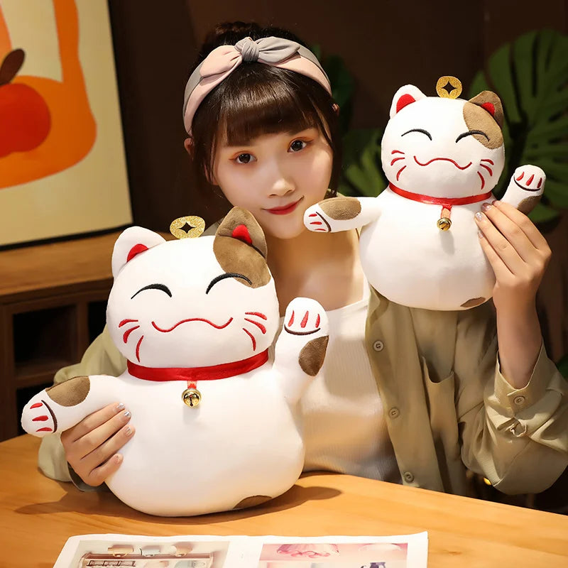 Person holding two large white cat-shaped kawaii plush toys with brown accents on a wooden table.