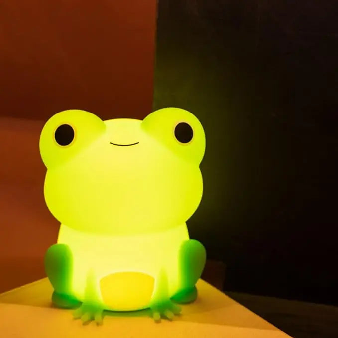 Green frog-shaped kawaii night light on a wooden surface with a dark background