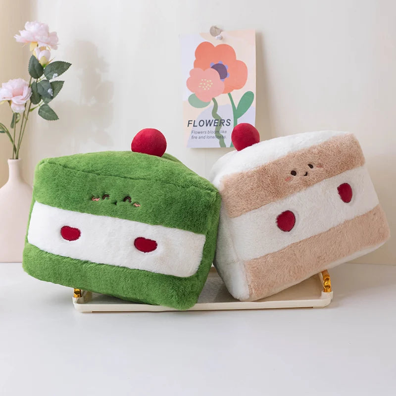 Two plush kawaii toys resembling cake slices on a white surface with a floral arrangement in the background.