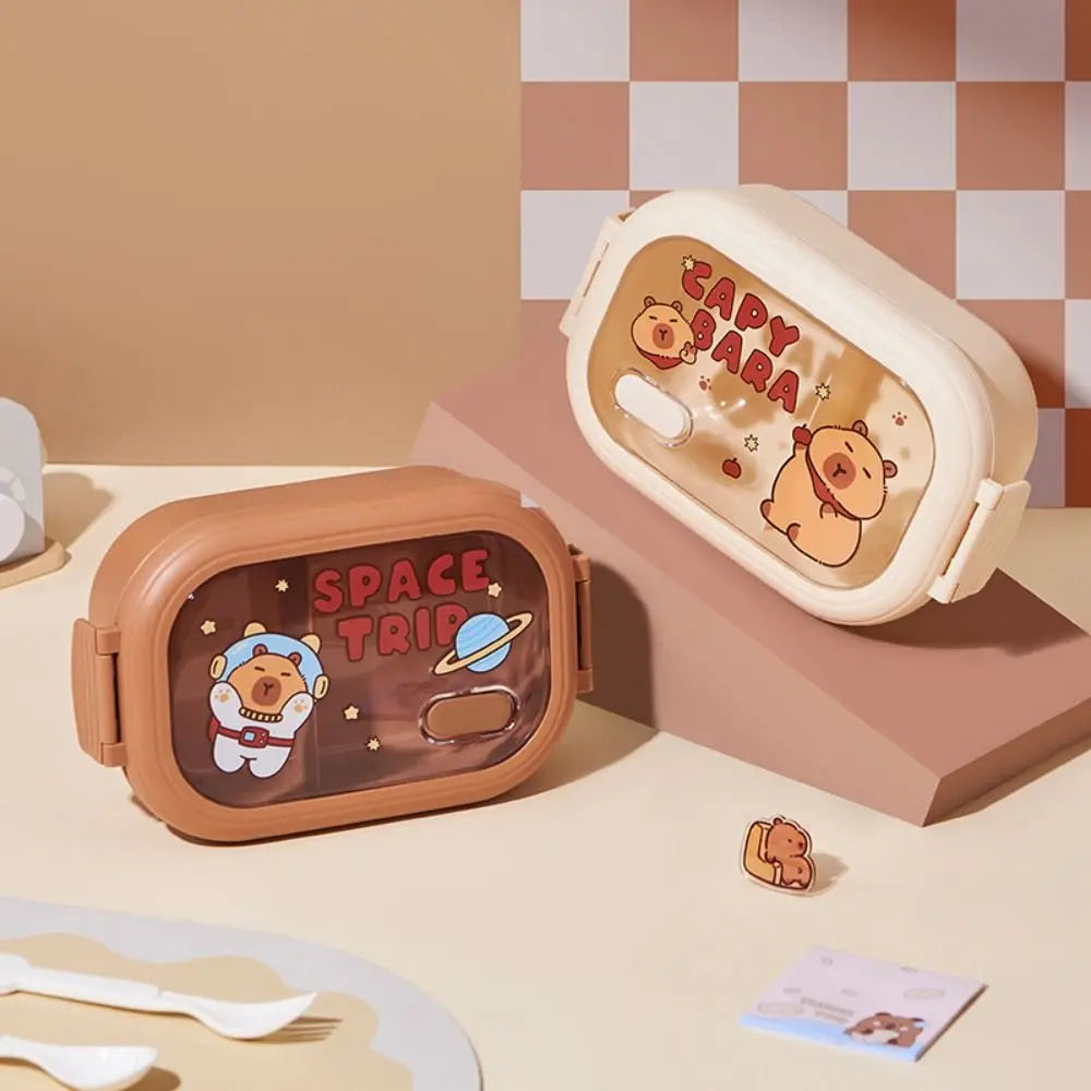 Two kawaii cartoon-themed lunch boxes with 'Capybara' and 'Space Trip' designs on a checkered background.