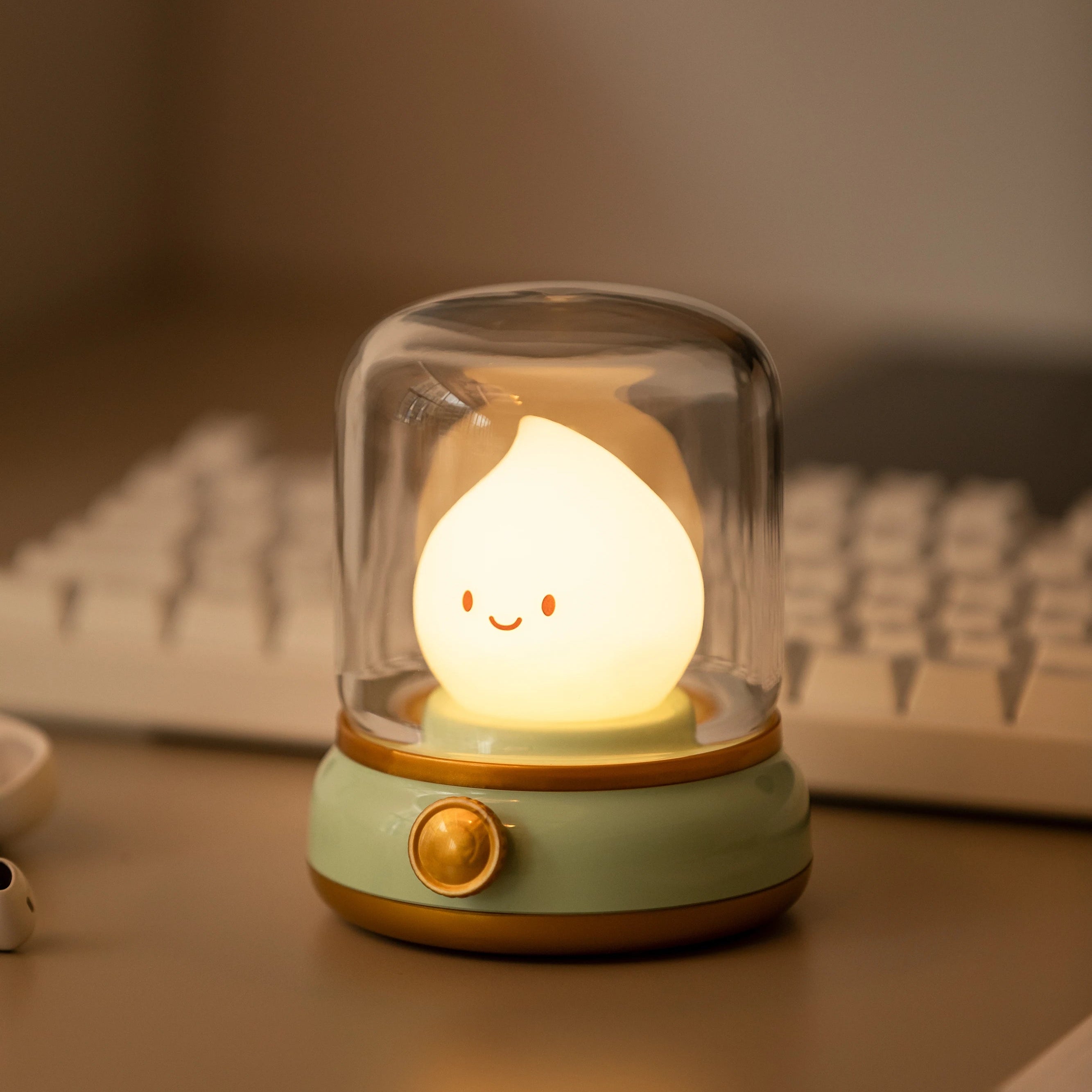 Small lamp with a kawaii smiling face under a glass dome on a desk with a keyboard in the background