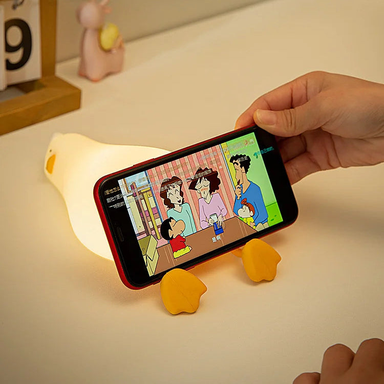 Person holding a smartphone with a cartoon displayed, using a yellow kawaii phone stand on a light surface.
