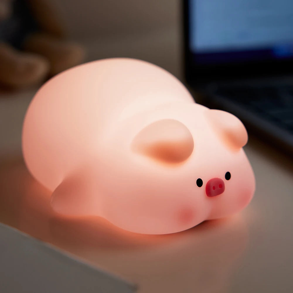 Pink pig-shaped kawaii night light on a desk with a blurred laptop in the background