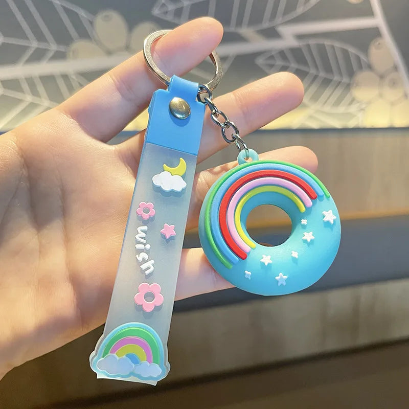 Colorful kawaii rainbow-themed keychain with a clear strap featuring cloud and flower designs, held by a hand.