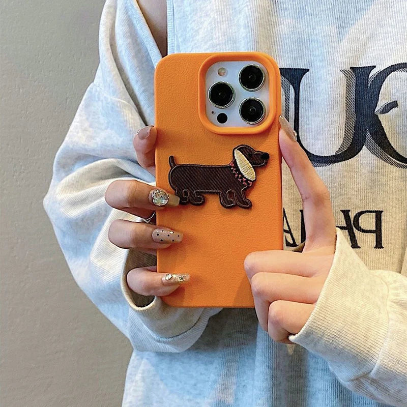 Person holding an orange phone case with a kawaii dachshund design, wearing a light gray sweatshirt.