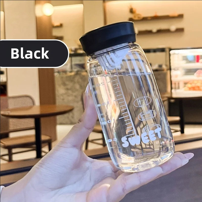 Clear Kawaii water bottle with black lid held in a hand, blurred indoor background