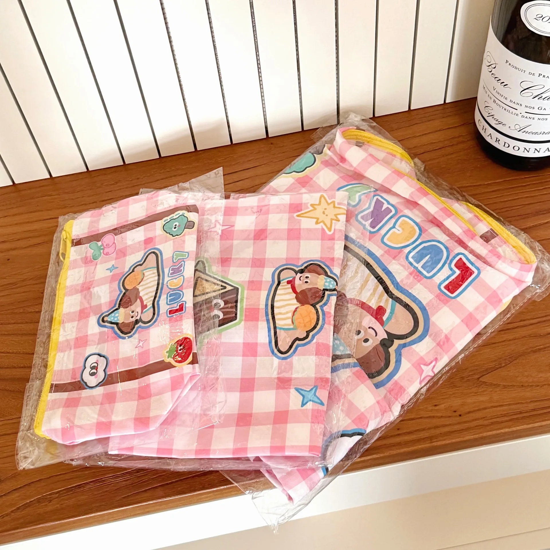 Packaged pink checkered napkins with Kawaii cartoon characters on a wooden surface.