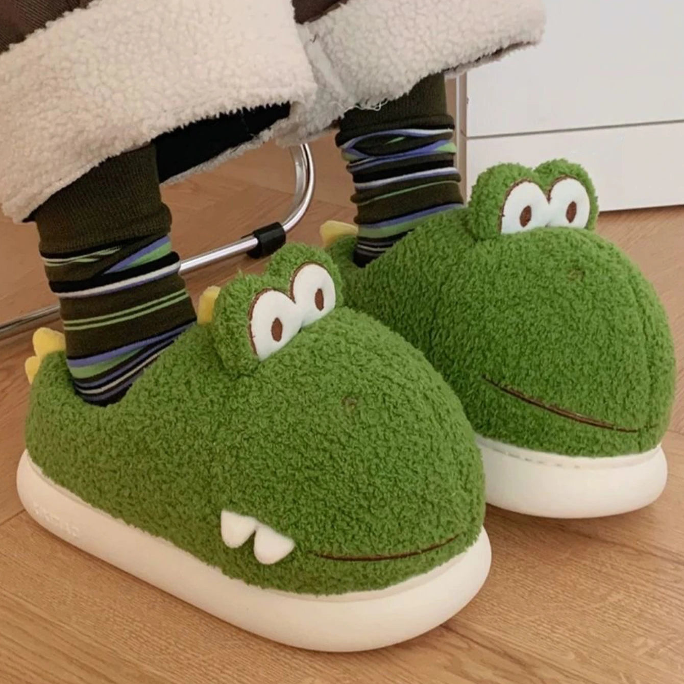 Green frog-shaped kawaii slippers worn by a person on a wooden floor.