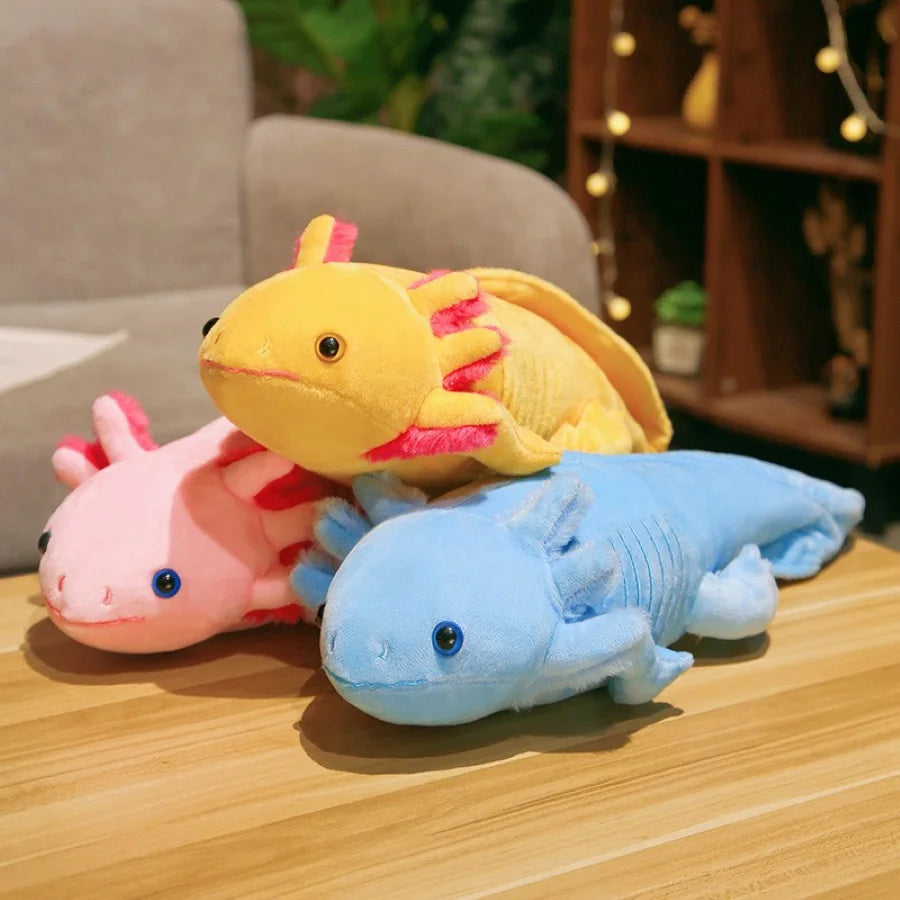 Three colorful axolotl kawaii plush toys stacked on a wooden surface with a blurred indoor background.