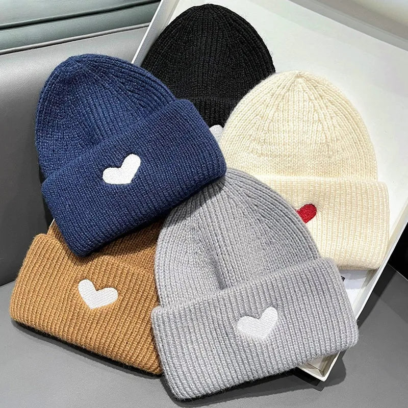 Five Kawaii knit hats in blue, black, beige, gray, and brown with heart designs on a white surface.