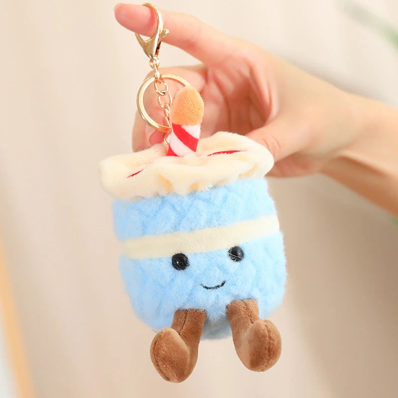 Plush keychain shaped like a blue creature with a kawaii smiling face, held by a hand against a neutral background.