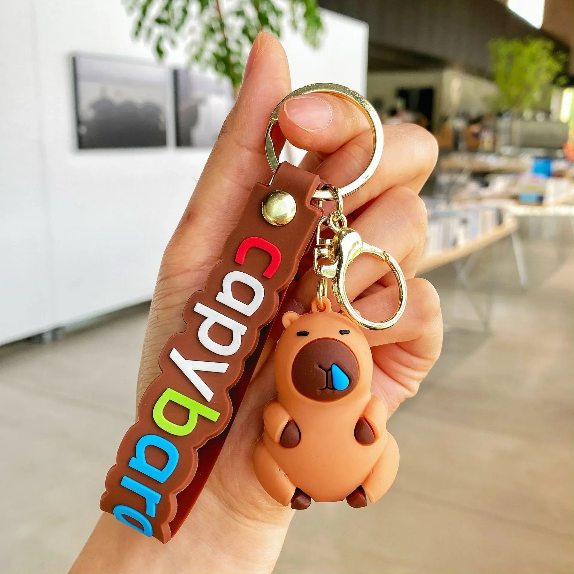 Hand holding a kawaii keychain with a bear design and colorful text in an indoor setting