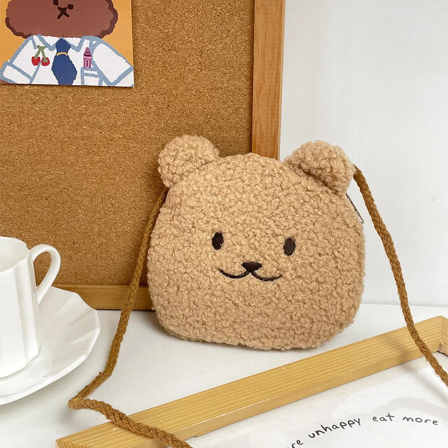Brown Kawaii teddy bear-shaped pouch on a white surface with a cork board and tea set in the background.