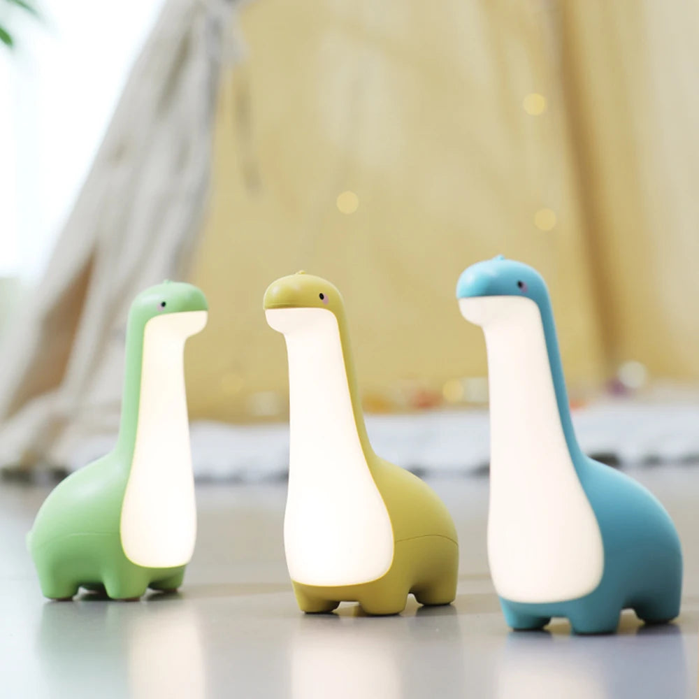Three dinosaur-shaped kawaii night lights in green, yellow, and blue on a light surface.