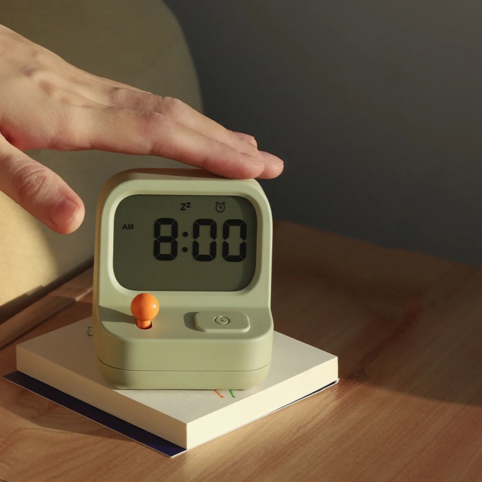 Green kawaii digital clock with a hand pressing the button on a wooden surface