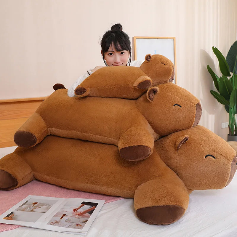 Large brown hippo-shaped kawaii cushion on a bed with a person partially visible behind it.