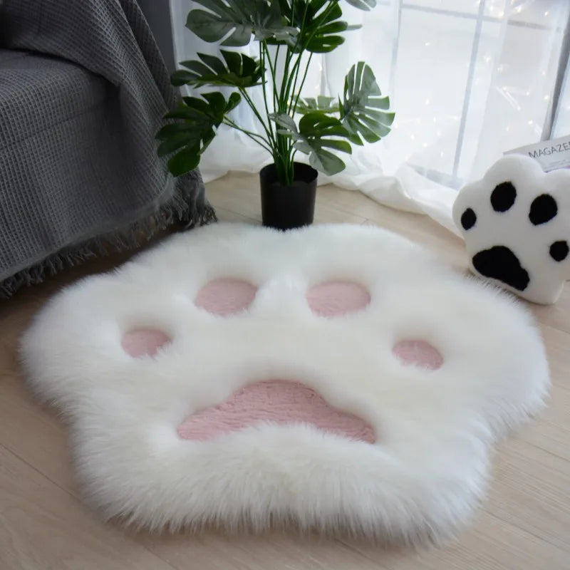 Fluffy kawaii paw-shaped cushion on a wooden floor with a plant and blanket in the background