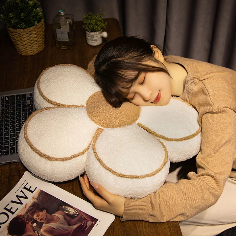 Person lying on a large flower-shaped kawaii pillow with a laptop and magazine on a table.