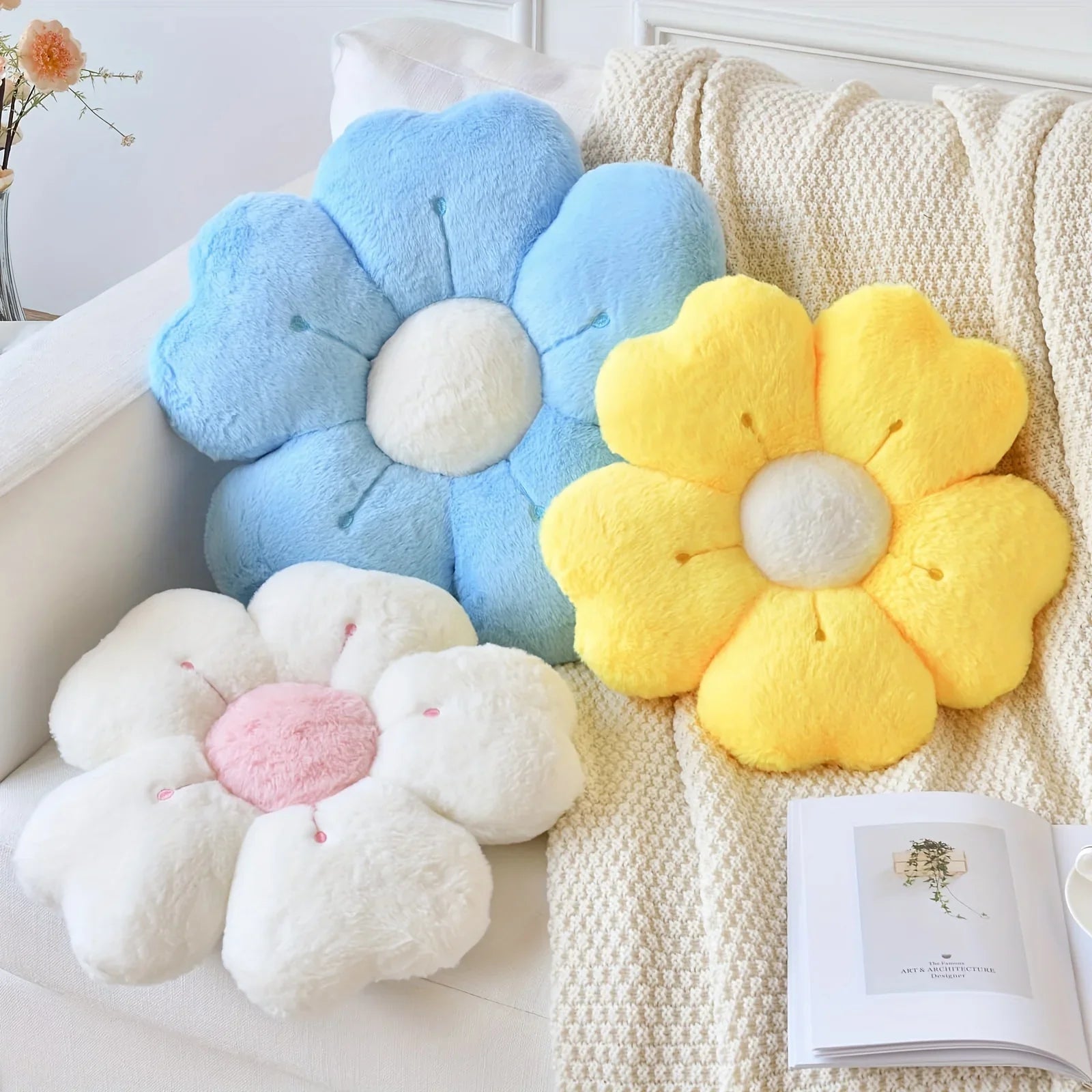 Flower-shaped kawaii cushions in blue, yellow, and white on a couch with a blanket and book.