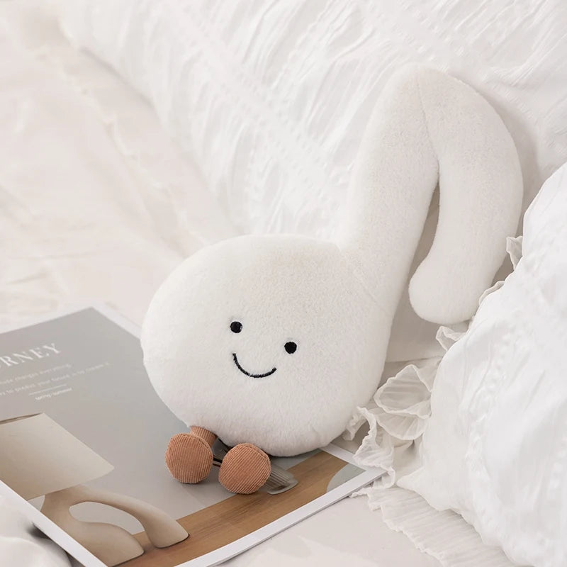 White plush kawaii toy with a smiley face on a bed with books and a lamp.