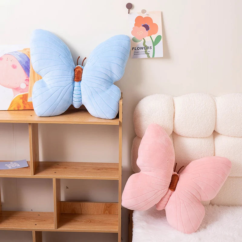 Butterfly-shaped kawaii cushions in blue and pink on a shelf and against a wall.