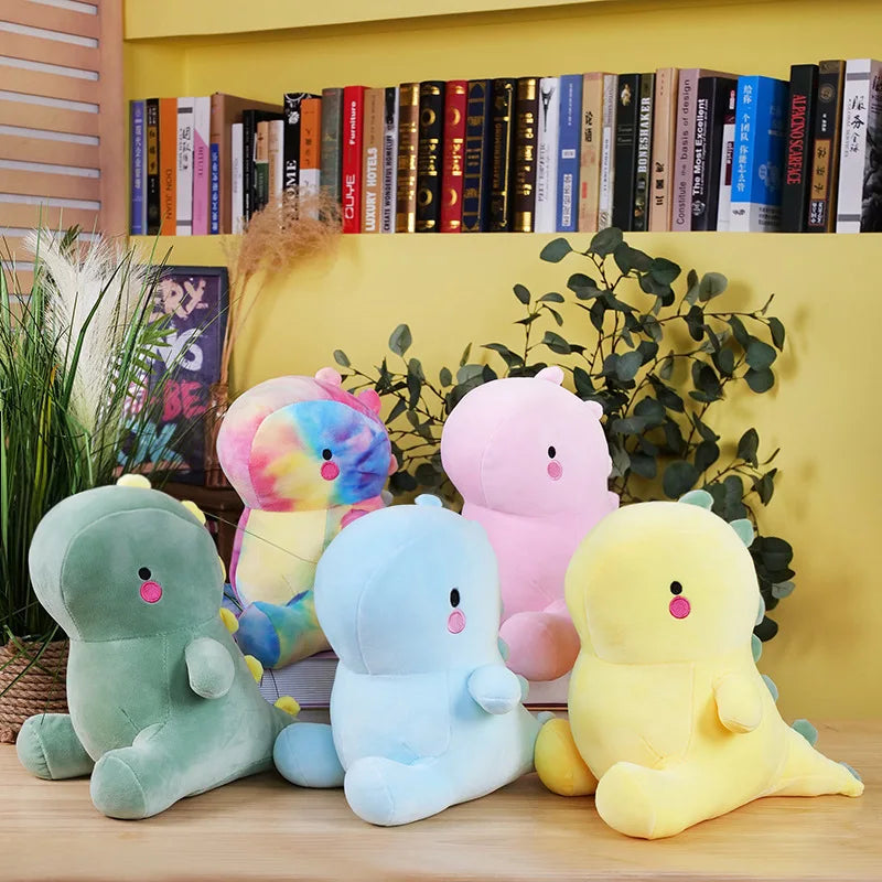 Five colorful kawaii plush toys on a wooden surface with a bookshelf and plants in the background.