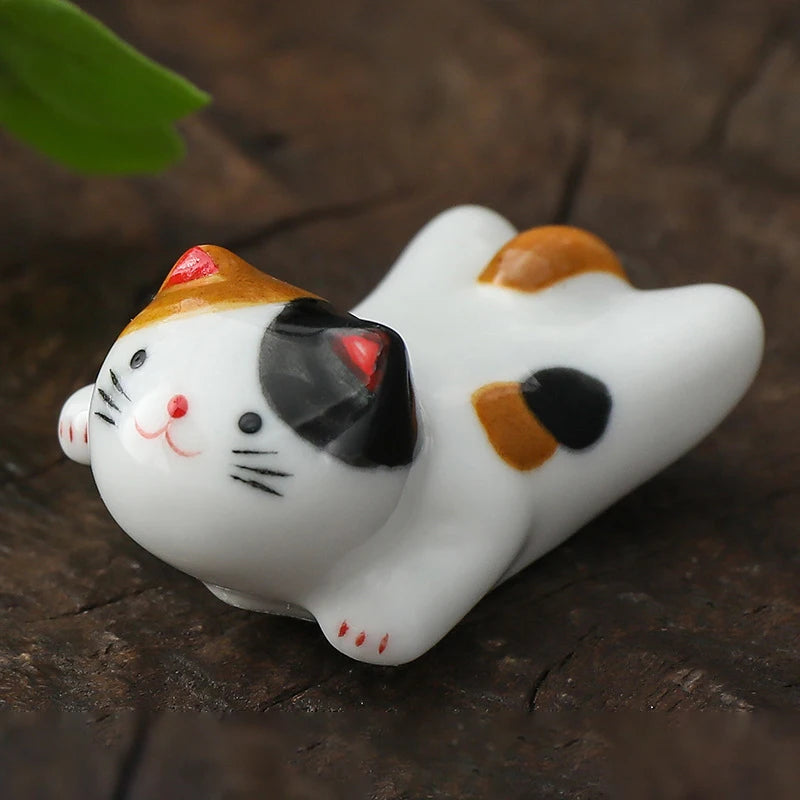 White ceramic kawaii cat figurine with black and orange spots on a wooden surface