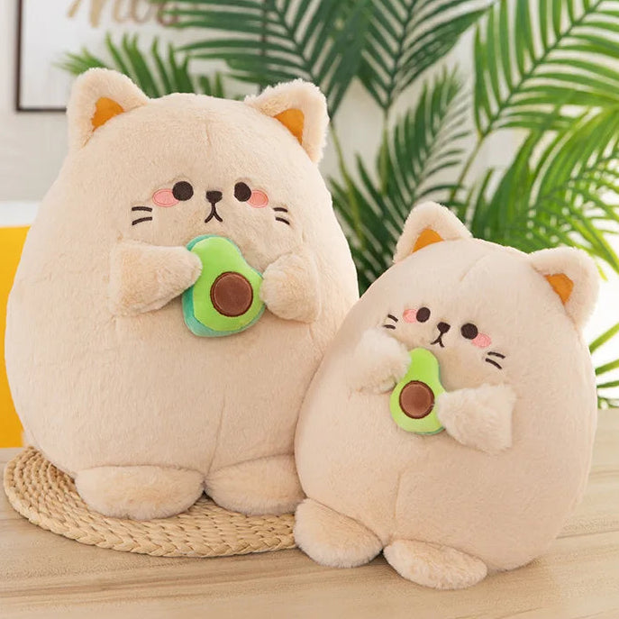 Two kawaii plush toys resembling cats holding avocados on a woven mat with a plant in the background.