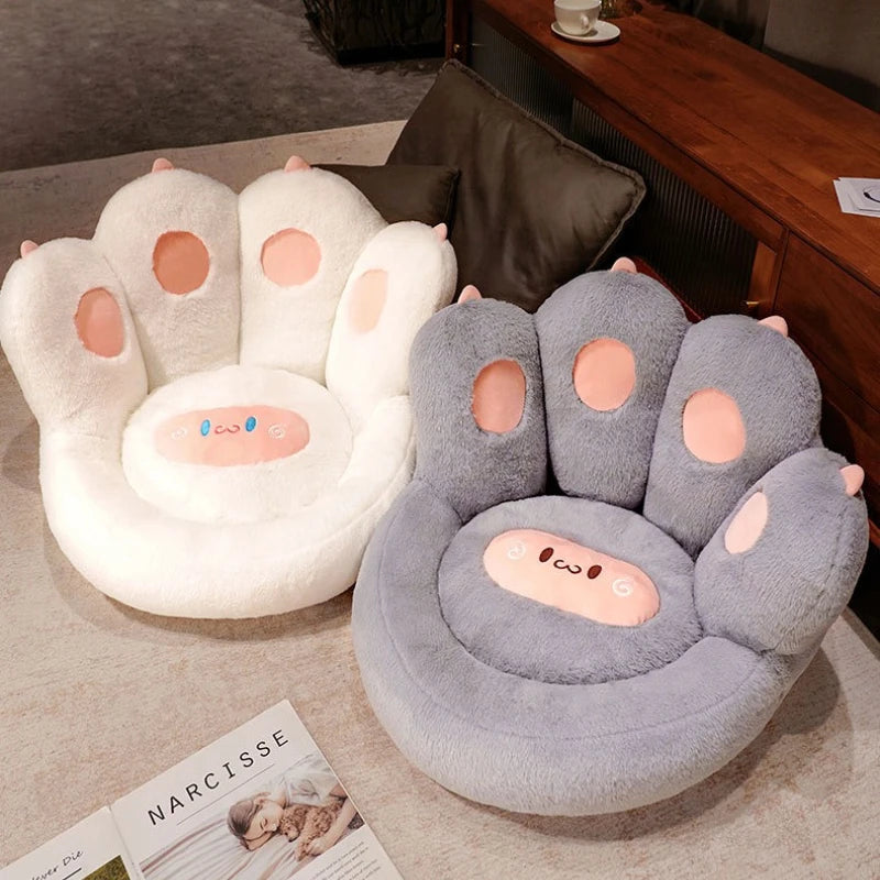 Two paw-shaped kawaii cushions, one white and one gray, on a couch with a magazine underneath.