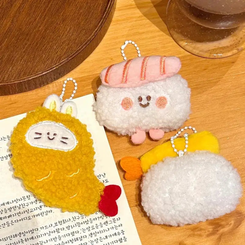 Three plush kawaii keychains on a wooden surface with a book underneath
