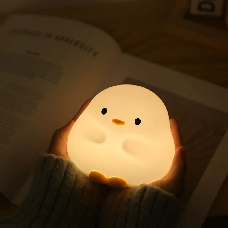 Person holding a glowing chick-shaped kawaii night light over an open book
