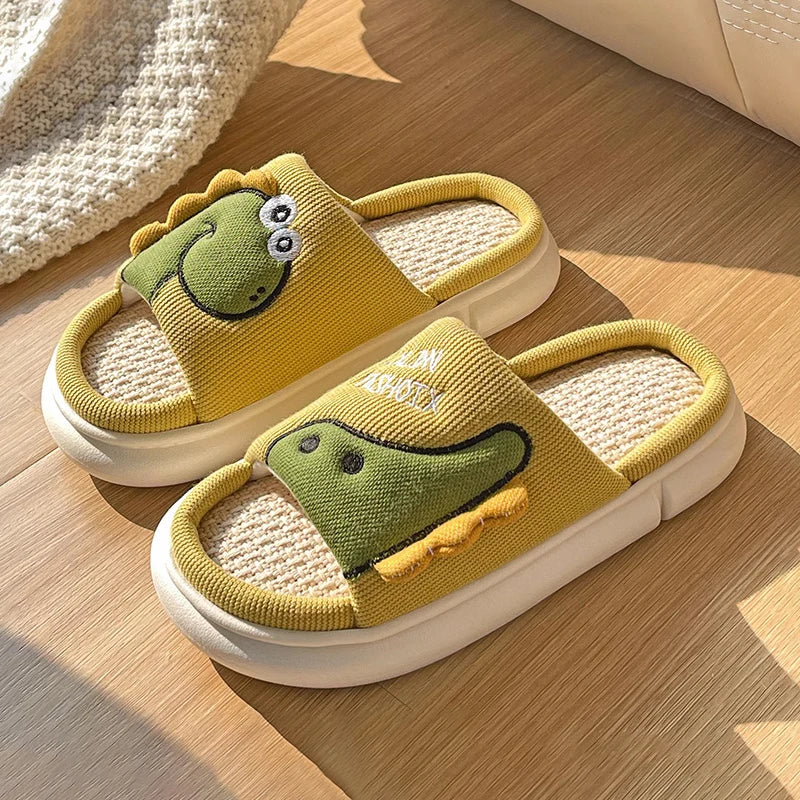 Pair of yellow slippers with kawaii green dinosaur faces on a wooden floor.