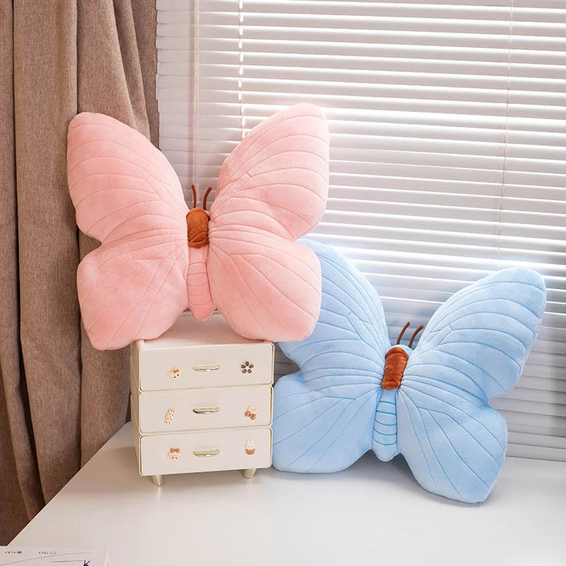 Pink and blue butterfly-shaped kawaii cushions on a white surface with a window in the background.