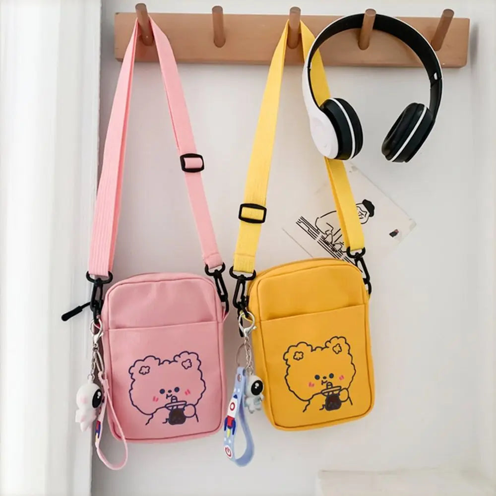 Pink and yellow crossbody bags with Kawaii cartoon designs on a white wall.