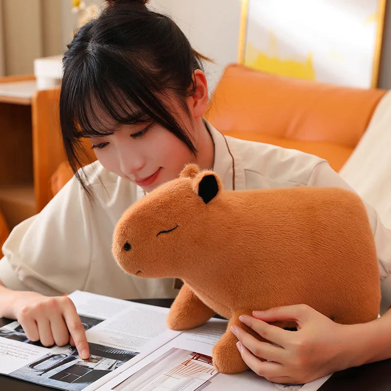 Woman reading a magazine with a kawaii plush capybara toy on a table.