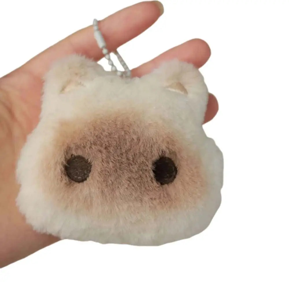 Plush kawaii keychain shaped like a dog's face held in a hand against a white background