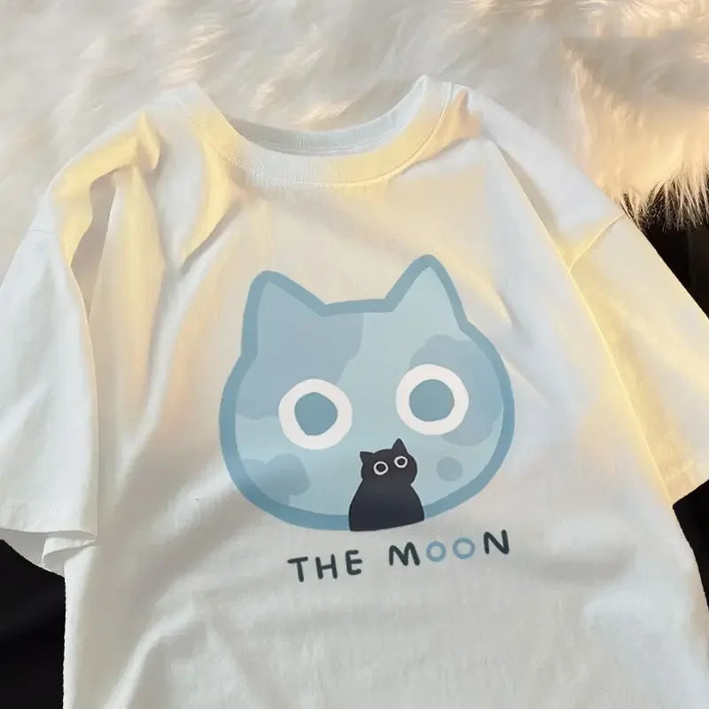 White t-shirt with a kawaii graphic of a cat sitting inside a moon, with 'The Moon' text, against a fur background.