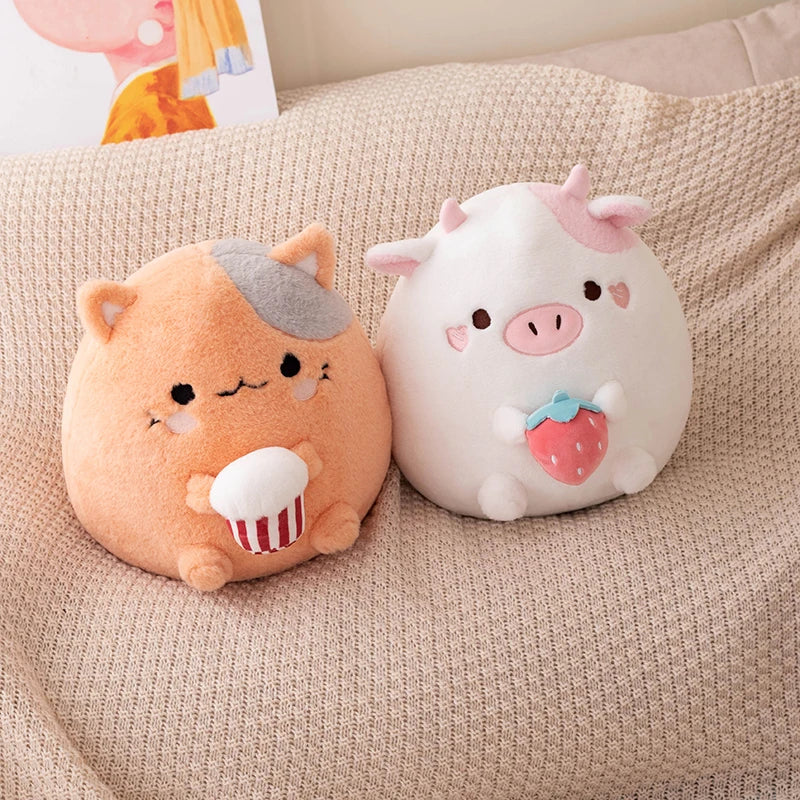 Two kawaii plush toys, one resembling a pig with a strawberry and the other resembling a cat with a cupcake, sitting on a beige surface.