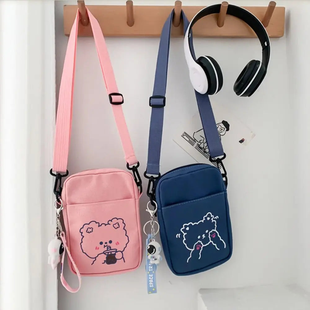 Pink and blue crossbody bags with Kawaii cartoon designs hanging on a hook, with headphones above them.
