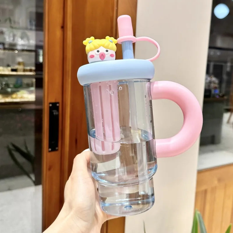 Clear Kawaii-style water bottle with pink handle and straw, held in a hand indoors.