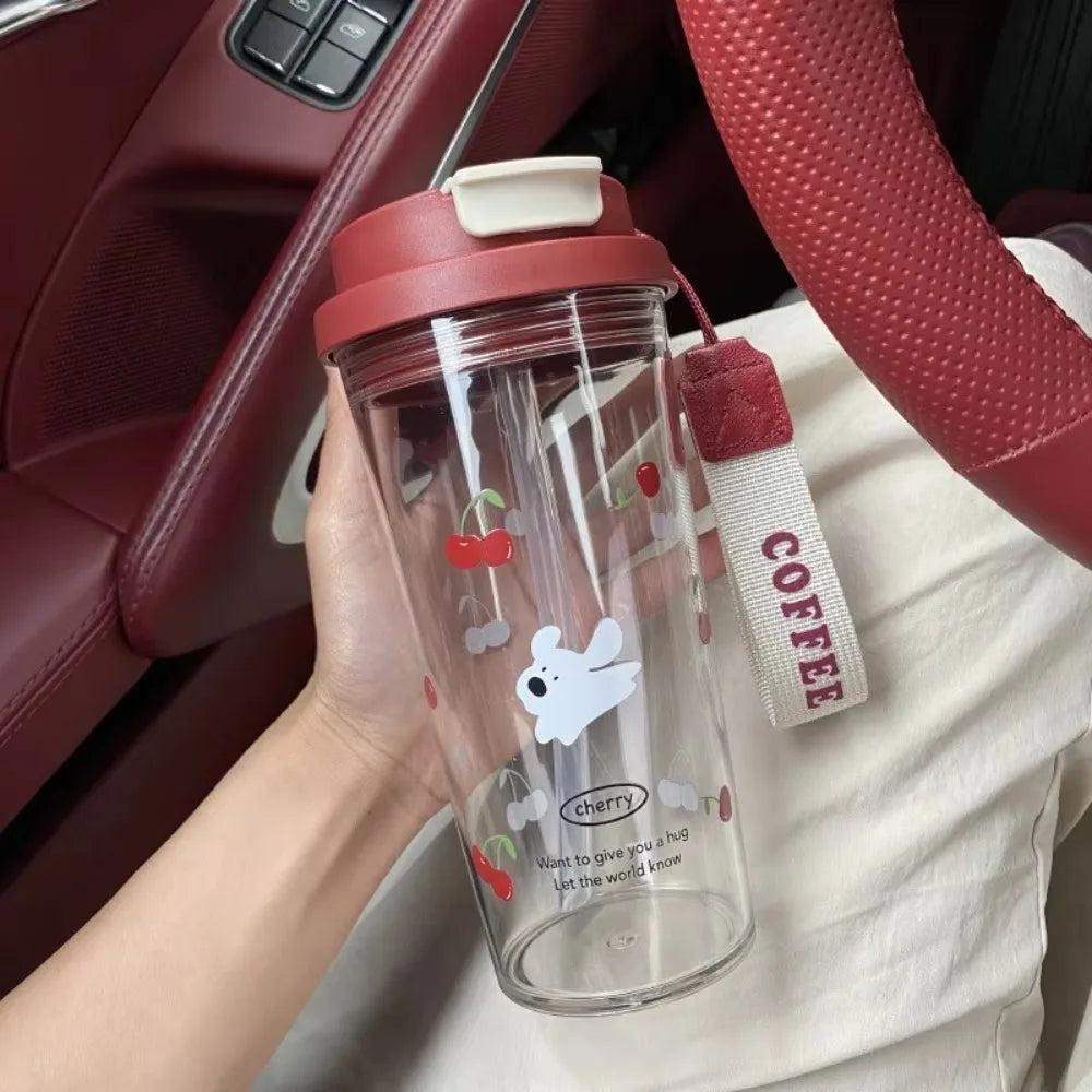 Clear tumbler with red lid and Kawaii cherry design held inside a car.