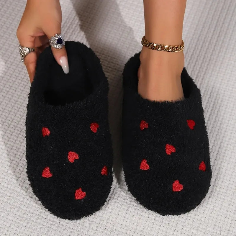 Black slippers with red heart kawaii patterns held by a hand on a textured surface