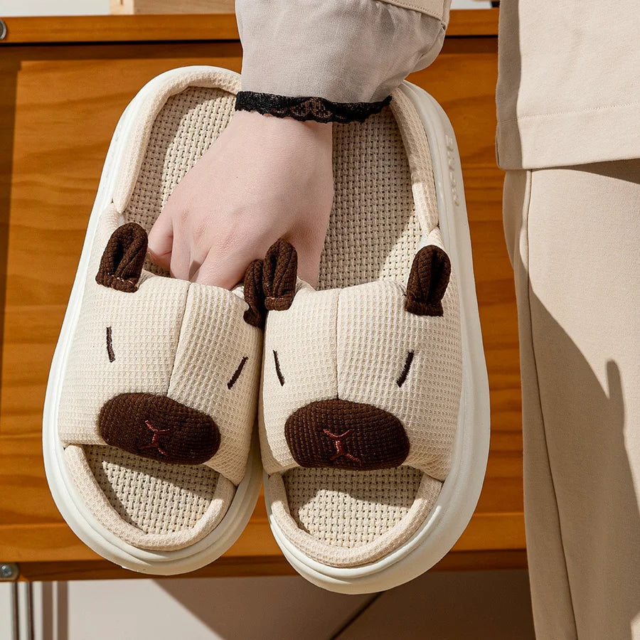 Pair of kawaii animal-themed slippers with a hand holding one, on a wooden floor.