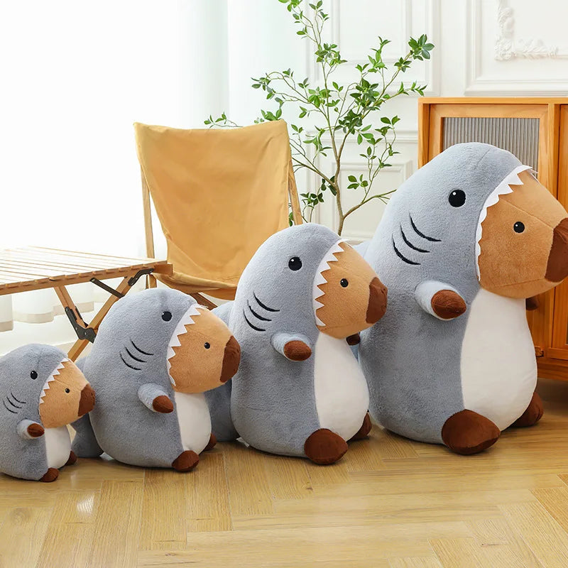 Set of shark-shaped kawaii plush toys on a wooden floor with a plant and chair in the background.