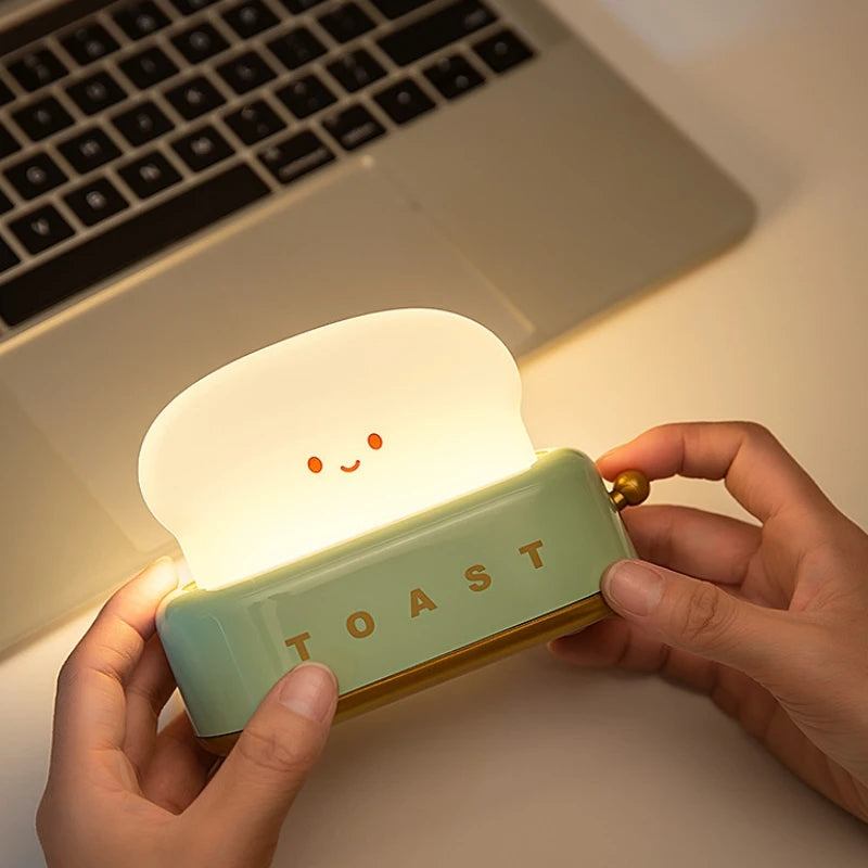 Light-up kawaii toaster-shaped night light held by hands with a laptop in the background