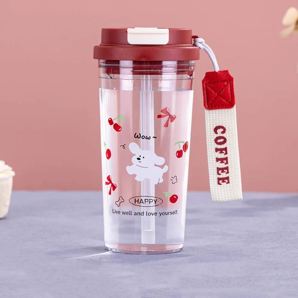 Clear tumbler with red lid and straw holder, featuring cartoon Kawaii designs and text, on a pink background.