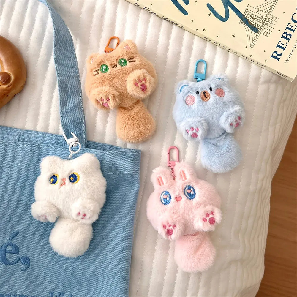 Four fluffy kawaii animal keychains hanging on a blue bag with a book in the background.