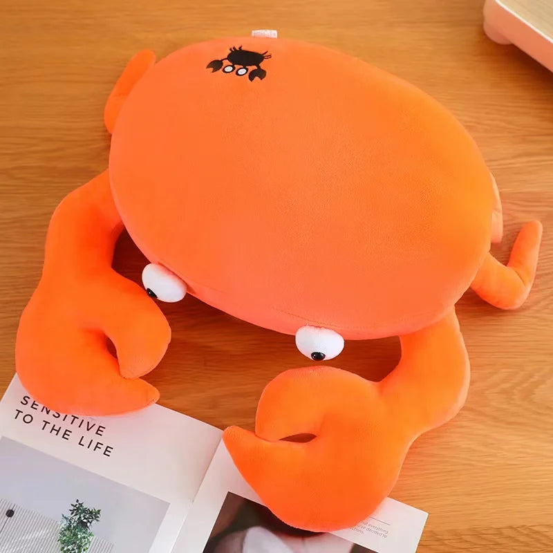 Orange crab-shaped kawaii cushion on a wooden surface with an open book underneath.